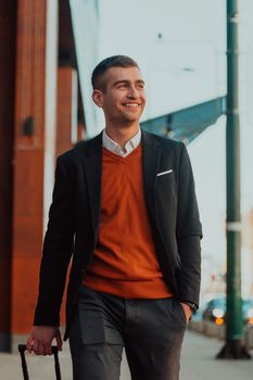 Going to the airport terminal. Young confident businessman traveler walking on city streets and pulling his suitcase drinking coffee and speaking on a smartphone. High quality photo