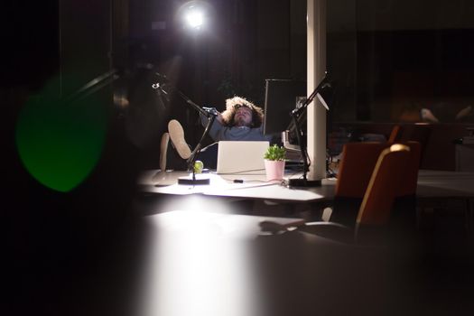 Full length of a relaxed casual young businessman sitting with legs on desk at night office