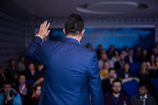 rear view of young successful businessman at business conference room with public giving presentations. Audience at the conference hall. Entrepreneurship club