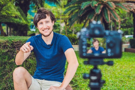 Young man blogger records video in front of the camera in the park. Blogger concept