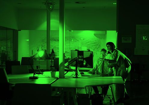 Two young designers are working on a new project in the night office using modern technology