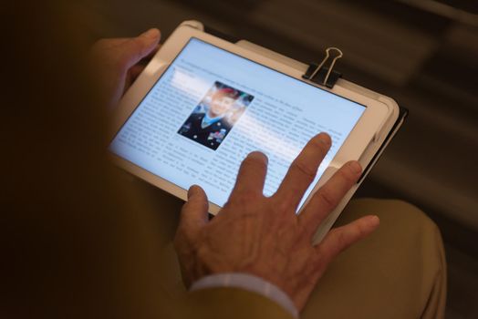 Closeup of mature hands holding tablet. Teacher with students in classroom