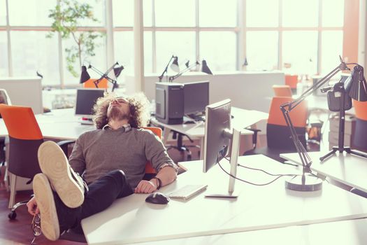 Full length of a relaxed casual young businessman sitting with legs on desk at office