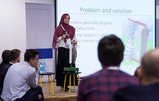 young muslim businesswoman with red scarf at business conference room giving public presentations. Audience at the conference hall. Entrepreneurship club