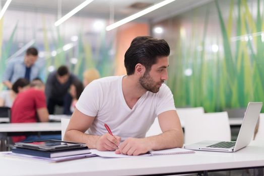 male student in classroom working  homework  and learning with laptop computer, students group in background