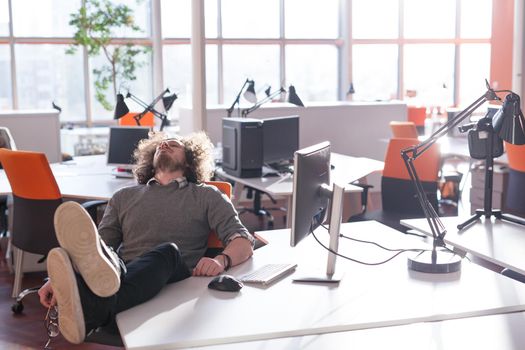 Full length of a relaxed casual young businessman sitting with legs on desk at office