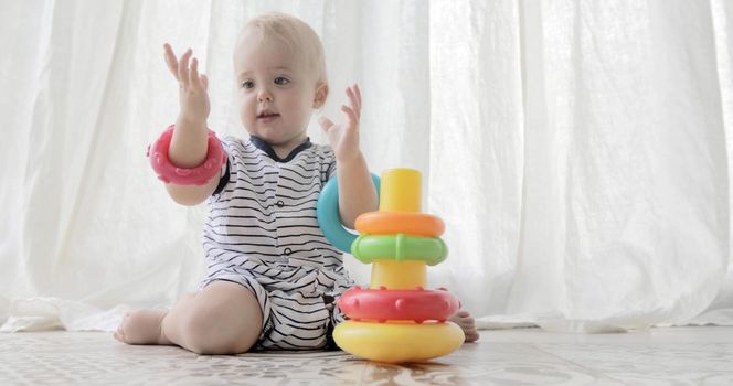 Charming toddler sitting on floor playing happily with plastic rings on white background