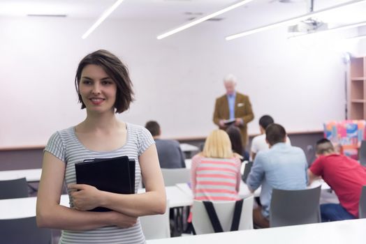 portrait of happy female student holding tablet while teacher teaching students in school classroom