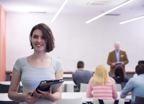 portrait of happy female student holding tablet while teacher teaching students in school classroom