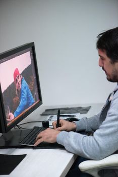 creative worker, photo editor working on graphic tablet at his desktop computer at small startup office