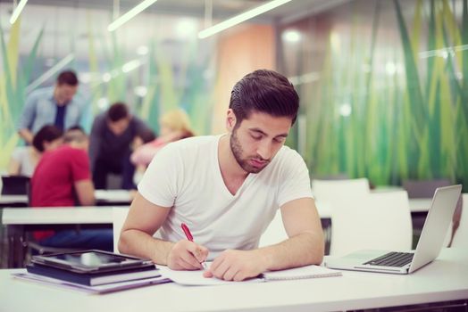 male student in classroom working  homework  and learning with laptop computer, students group in background