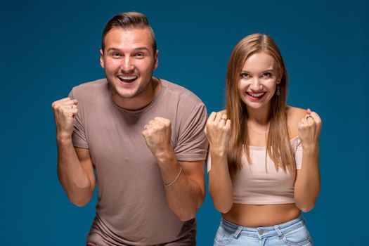 Overjoyed woman and man raise fists with triumph, have successful deal, exclaim joyfully, on blue background. People, collaboration and success concept. Hooray, we did it finally