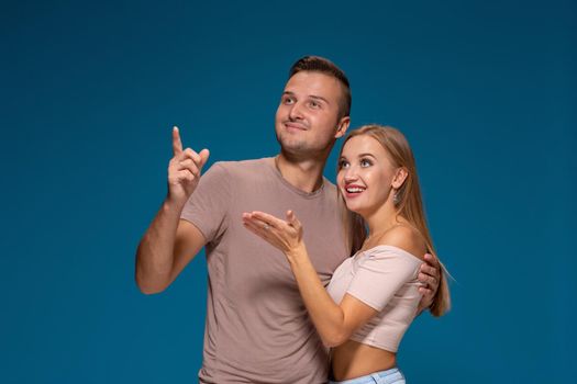 Portrait of the happy couple looking and pointing into the distance, isolated on blue background. Emotional young couple laughing at something