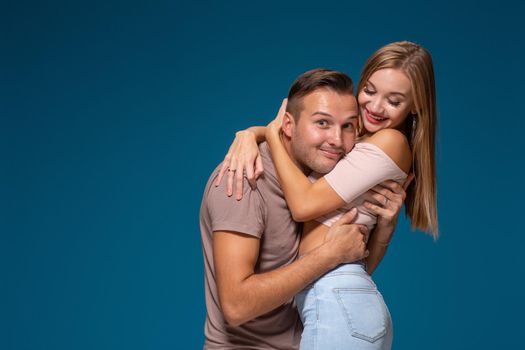 Young couple is hugging on blue background in studio. They wear T-shirts, jeans and smile. Friendship, love and relationships concept