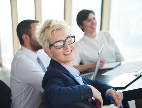 blonde with short hairstyle  and glasses,  business woman on meeting, people group in background at modern bright office indoors