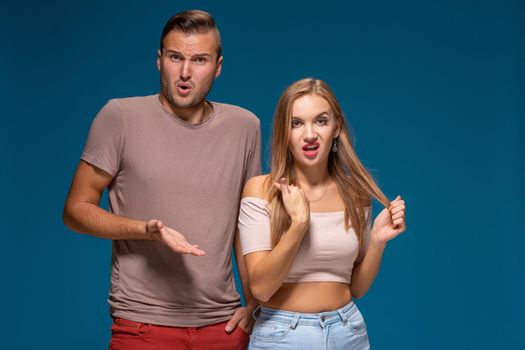 Portrait of clueless young man and woman making confused gestures while posing in studio together, being lost for words, looking at camera in indignation and irritation