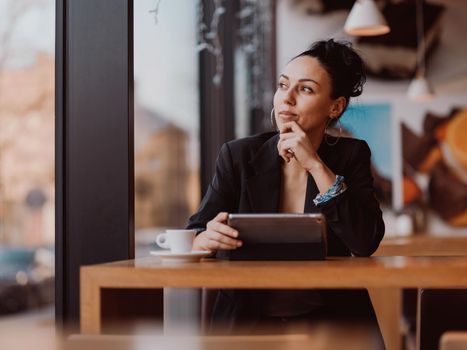 Latina woman sitting in cafe using tablet and drinks coffee on break from work