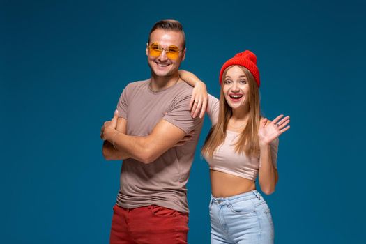 Studio lifestyle portrait of two best friends hipster wearing stylish bright outfits, hats, denim shorts and glasses, going crazy and having great time together. Indoor studio shot, isolated on blue background.