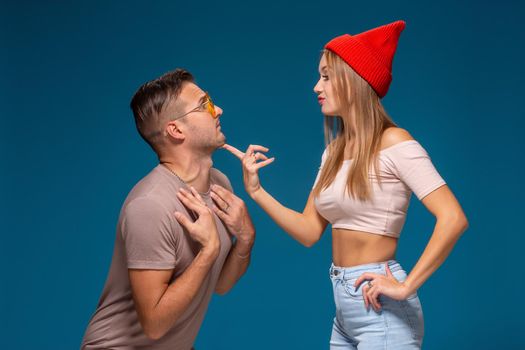 Studio lifestyle portrait of two best friends hipster wearing stylish bright outfits, hats, denim shorts and glasses, going crazy and having great time together. Indoor studio shot, isolated on blue background.