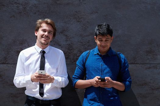 casual multiethnic startup business men one of them is indian using mobile phone during break from work in front of gray wall outside