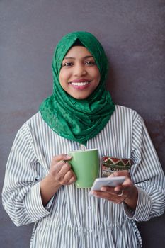 african muslim businesswoman with green hijab using mobile phone during coffee break from work in front of gray wall outside