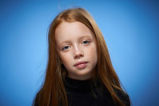 redhead girl with freckles on her face posing close-up blue background. High quality photo