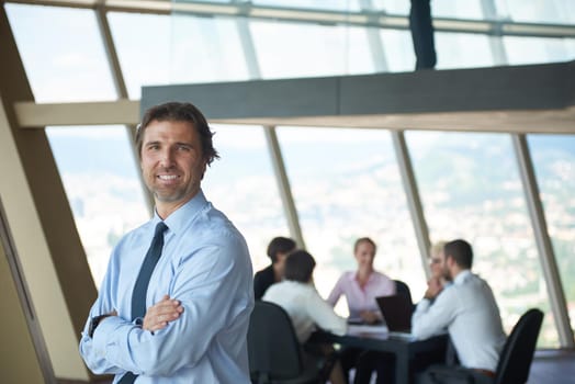 handosme business manportrait  at modern bright office indoors with his team in group working together in background