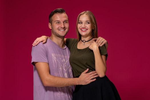 Young nice couple posing in the studio, express emotions and gestures, smiling, on a burgundy background with copy space for your advertisement or written text.