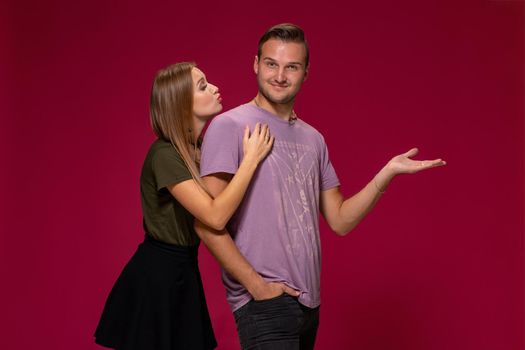 Young nice couple posing in the studio, express emotions and gestures, smiling, on a burgundy background with copy space for your advertisement or written text.