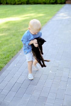 Little blond playing with black cat outdoors. Concept of childhood and pets.
