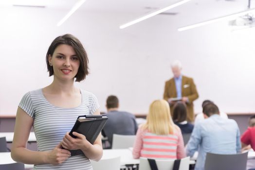 portrait of happy female student holding tablet while teacher teaching students in school classroom