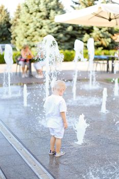 Little male baby standing near fountain. Concept of walking in city with children.