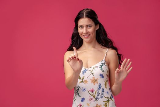Smiling serious girl holding her index finger in front, saying: hey, wait a minute on the pink background