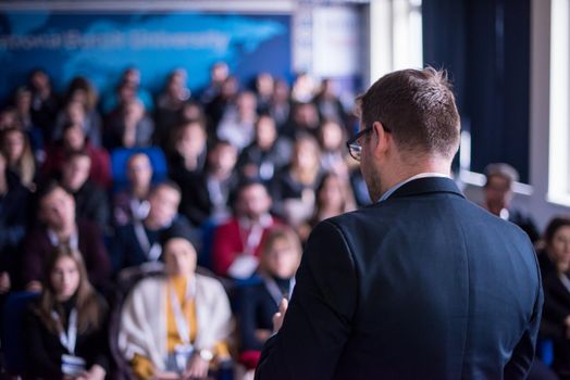 rear view of young successful businessman at business conference room with public giving presentations. Audience at the conference hall. Entrepreneurship club