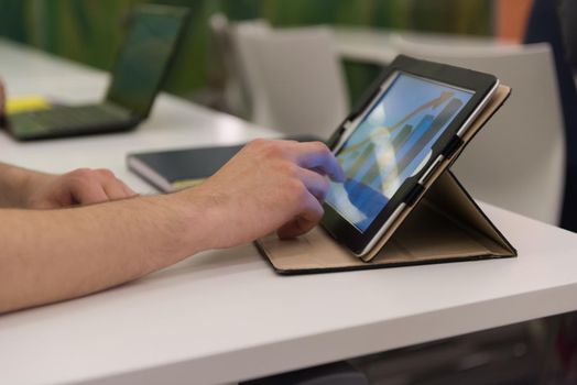 Closeup of mature hands holding tablet. Teacher with students in classroom