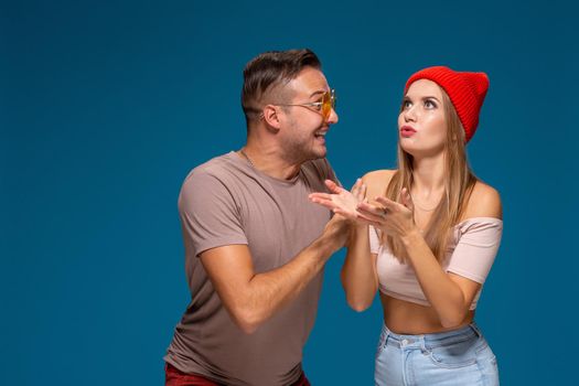 Surprised couple in casual clothes pointing with their index fingers up looking there with great astonishment isolated over blue background with copy space for your advertisement or written text.