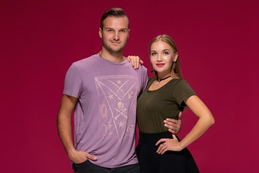 Young nice couple posing in the studio, express emotions and gestures, smiling, on a burgundy background with copy space for your advertisement or written text.