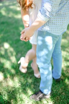 Closeup guy and girl holding hands in grass background. Concept of relationships and love.