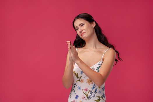 A close up image of a beautiful woman praying with her hands foldedand on the pink background