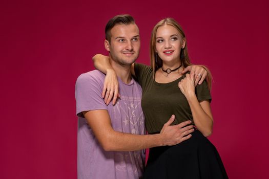 Young nice couple posing in the studio, express emotions and gestures, smiling, on a burgundy background with copy space for your advertisement or written text.