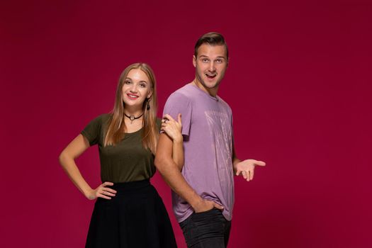 Young nice couple posing in the studio, express emotions and gestures, smiling, on a burgundy background with copy space for your advertisement or written text.