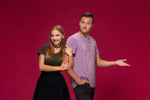 Young nice couple posing in the studio, express emotions and gestures, smiling, on a burgundy background with copy space for your advertisement or written text.