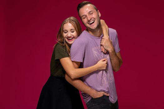 Young nice couple posing in the studio, express emotions and gestures, smiling, on a burgundy background with copy space for your advertisement or written text.