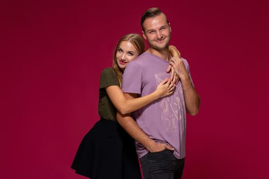 Young nice couple posing in the studio, express emotions and gestures, smiling, on a burgundy background with copy space for your advertisement or written text.