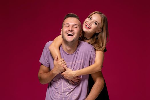 Young nice couple posing in the studio, express emotions and gestures, smiling, on a burgundy background with copy space for your advertisement or written text.