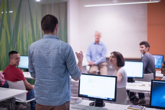 student answering a question in classroom, mature teacher and students in computer lab classroom