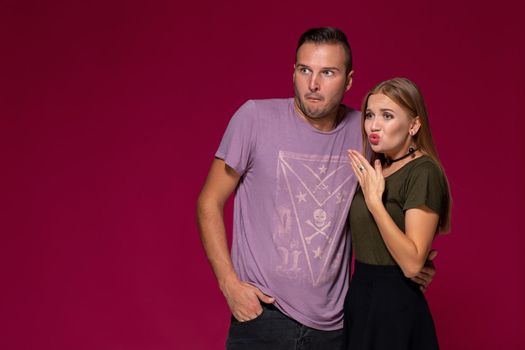 Unhappy discontent woman and man look with disgusting expression, as see something unpleasant. Friends express negative emotions and feelings, isolated over burgundy background. Awkward couple