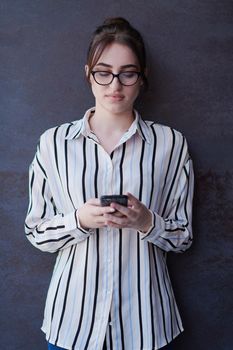 startup businesswoman in shirt with a glasses using mobile phone while standing in front of gray wall during break from work outside