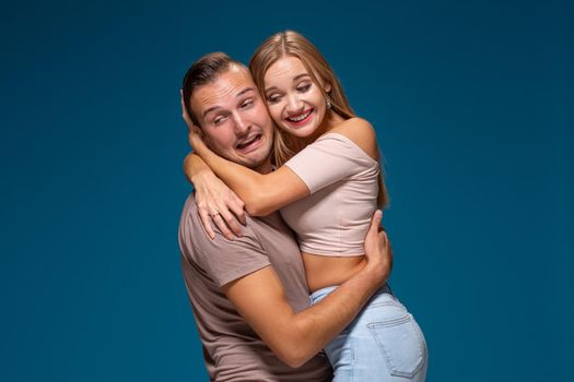 Young couple is hugging on blue background in studio. They wear T-shirts, jeans and smile. Friendship, love and relationships concept