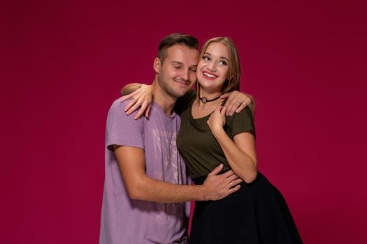 Young nice couple posing in the studio, express emotions and gestures, smiling, on a burgundy background with copy space for your advertisement or written text.